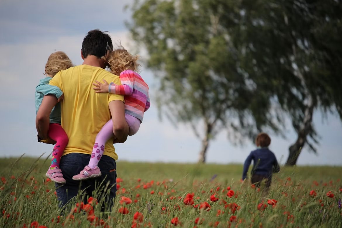 A father carrying his two children through a poppy field