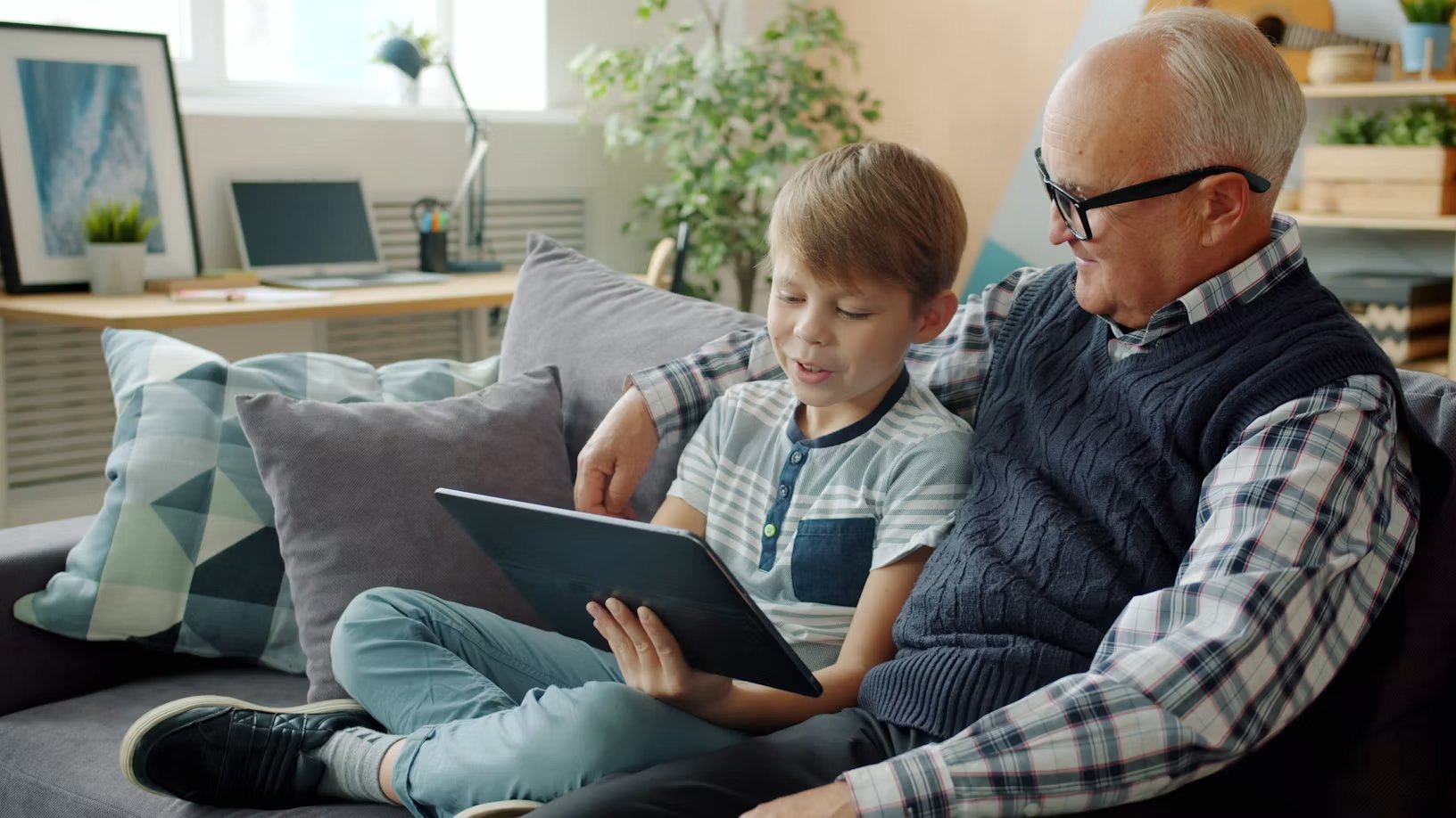 A grandfather and grandson reading together on a tablet on the sofa
