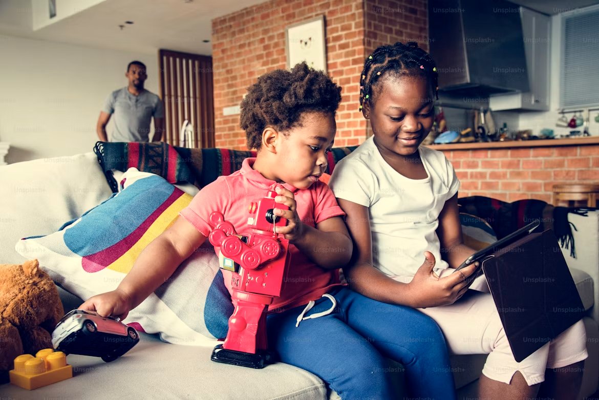 Two children playing and reading on a tablet on the sofa