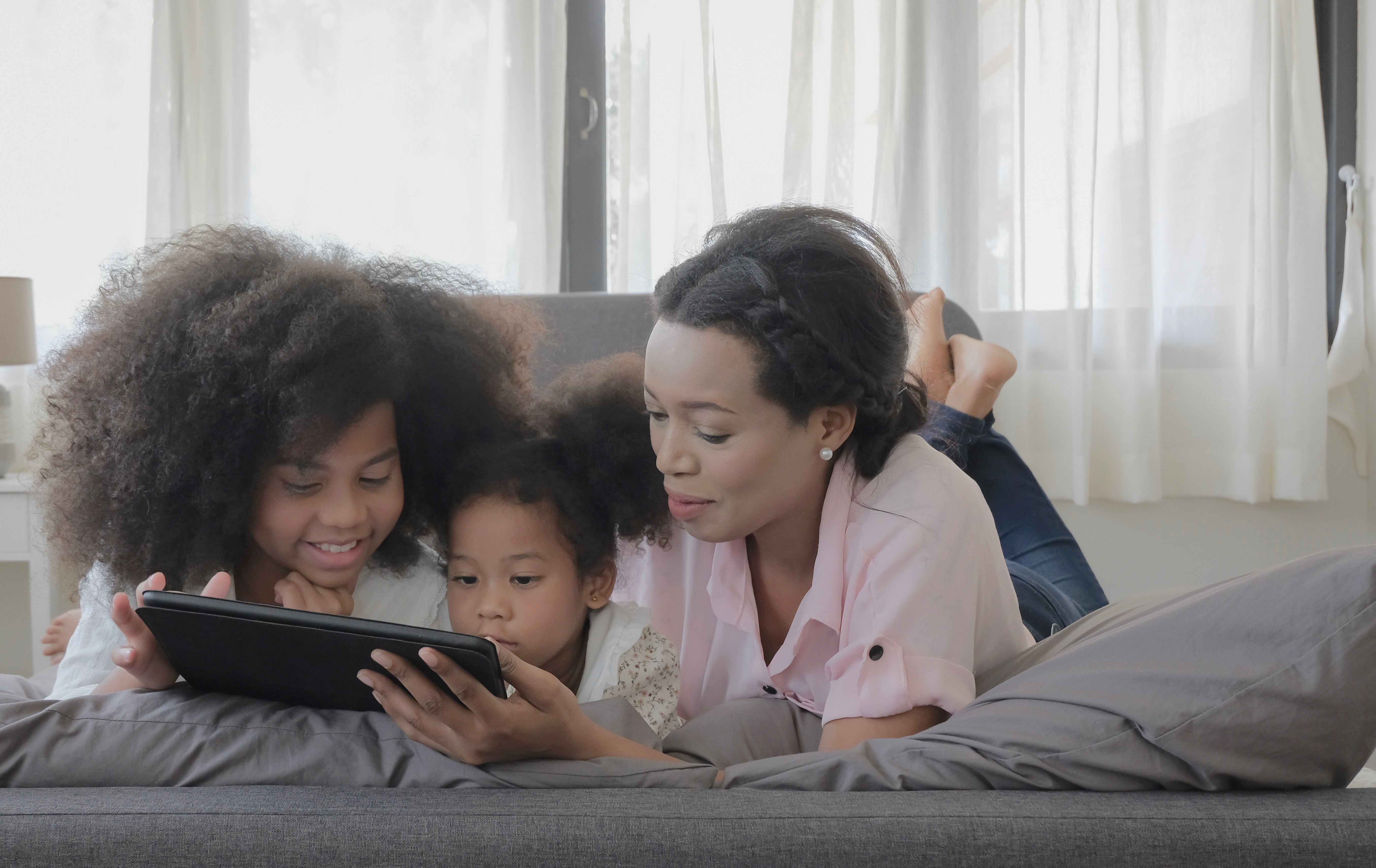 A mother and two children looking at a tablet together on the sofa