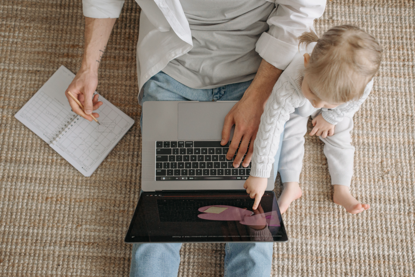 A parent working on a laptop at home with a small child on their lap