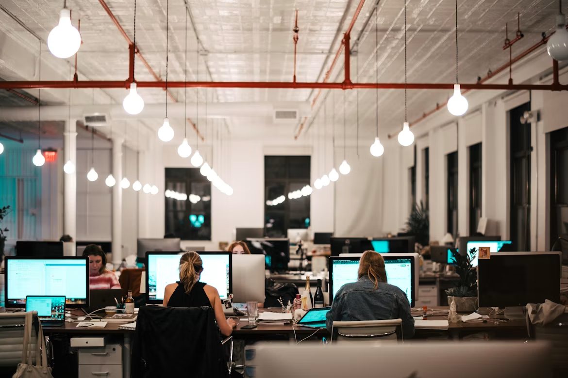 An open-plan office with people working at desks under hanging lights