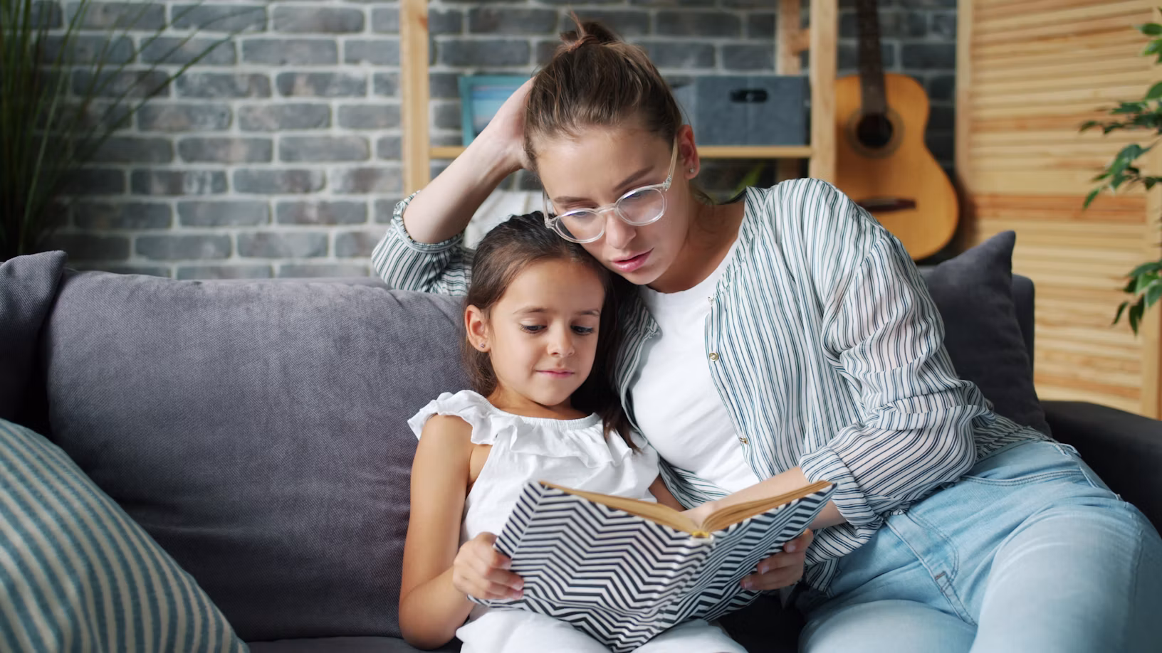 A mother and daughter reading a book together on the sofa