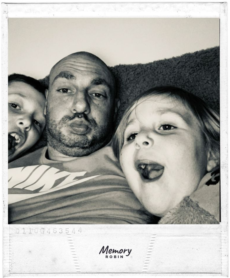 Simon with his two children lying together, pulling happy faces at the camera